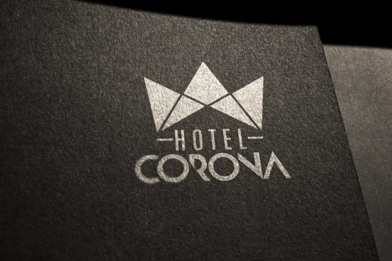 Logotipo de Hotel Corona con una corona geométrica, impreso en plata sobre papel oscuro texturizado